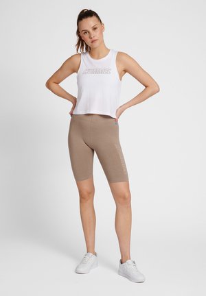 Kort wit tanktop met "HUMMEL" opdruk en beige fietsbroek. Beide kledingstukken hebben een getailleerd ontwerp. Witte sneakers maken de outfit af.