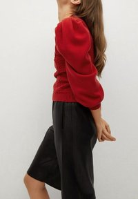 Pull en tricot rouge avec des manches ballon, des poignets côtelés et un motif texturé, assorti à un short en simili cuir noir avec une finition lisse.