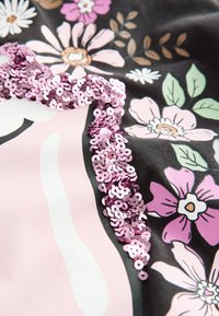 Svart tyg med ett blommönster i rosa, vitt och grönt, prytt med en rad glansiga rosa paljetter för textur och detalj.