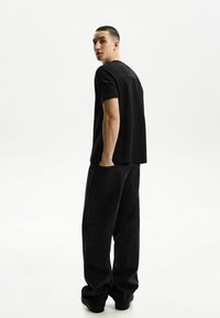 Schwarzes Baumwoll-T-Shirt mit kurzen Ärmeln und leichtem Drop-Shoulder, kombiniert mit lockeren schwarzen Denim-Jeans mit Gesäßtaschen.