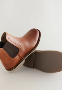 Stivale Chelsea in pelle marrone con lati elastici, punta arrotondata e suola in gomma testurizzata. Presenta una rifinitura di cuciture lungo i bordi.
