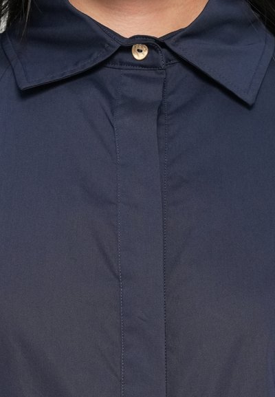 Camicia blu navy con colletto classico, chiusura a bottone singolo e dettagli di cuciture verticali. Realizzata in un tessuto liscio e leggero.