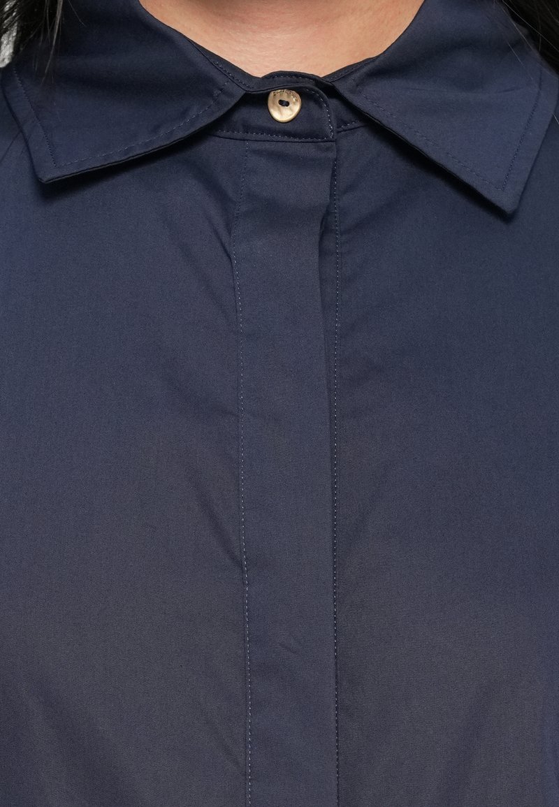 Chemise bleu marine avec un col classique, une fermeture à un bouton et des détails de coutures verticales. Fabriquée en tissu lisse et léger.