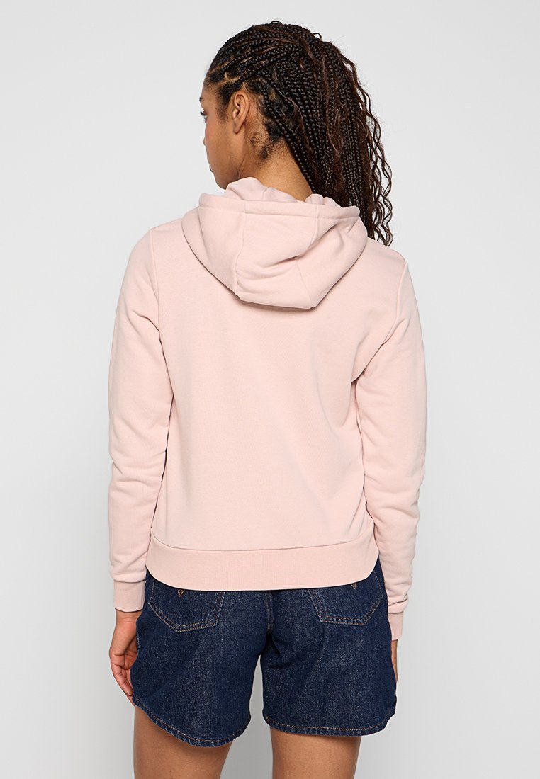 Felpa con cappuccio rosa dal tocco morbido, con polsini e orlo a costine, indossata con pantaloni corto in denim scuri. Nessun logo o motivo visibile.