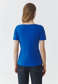Top corto blu royal a maniche corte con scollatura ampia e texture liscia. La parte posteriore ha un design attillato, abbinata a jeans di denim scuro.