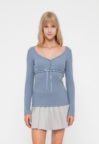 Blu deschis, bluză cu mânecă lungă, cu decolteu în V și închidere cu nasturi, având o talie decorativă din dantelă și accente albe de șnur.