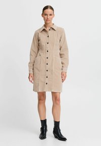 Beige kordflodress med långa ärmar, knappstängning fram och två sidofickor. Kombinerad med svarta ankelstövlar.