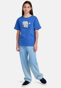 Blå bomulds T-shirt med et elefantmotiv og ordet "ELEMENT" nedenunder. Sammen med lyseblå denim bukser. Casual pasform.