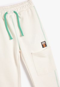 Crème kleurige sweatpants met groene trekkoorden en bijpassende stiksels. Beschikt over een zijzak en een merketiket. Zacht, casual ontwerp.