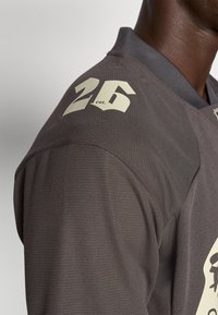 Tricou sportiv de culoare gri închis, cu un material texturat, având un număr alb "26" pe umărul drept și un guler cu bordură.