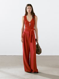 Rode ribbel tanktop en een broek met wijde pijpen met een strikceintuur. Een lange ketting met een hanger en een bruine tas maken de outfit compleet.