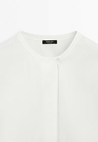 T-shirt blanc à col rond avec un seul bouton près du col et une étiquette noire indiquant "Massimo Dutti Made in China."
