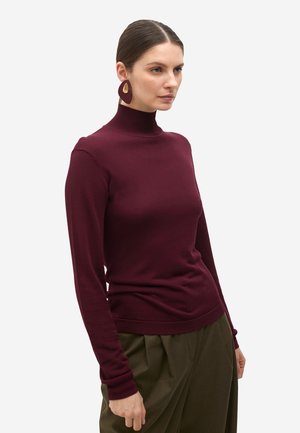 Suéter de cuello alto burdeos con mangas largas, una silueta ajustada y puños acanalados, combinado con pantalones oliva con pliegues.