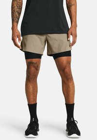 Pantalones cortos de hombre en caqui y negro. Capa exterior en caqui, capa interior en negro. Se complementan con calcetines deportivos negros y zapatillas. Tela texturizada.