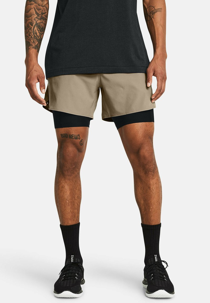 Pantalones cortos de hombre en caqui y negro. Capa exterior en caqui, capa interior en negro. Se complementan con calcetines deportivos negros y zapatillas. Tela texturizada.