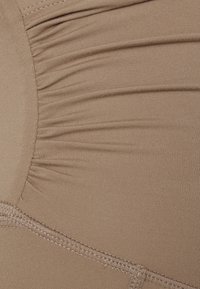 Beige kangas na hufaa na muundo laini na maelekezo yaliyojikusanya, ikiwa na mshono wa kushona tofauti kwenye kingo za chini.