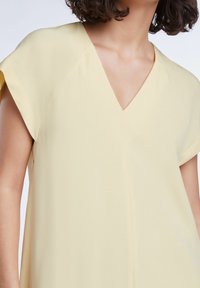 Geel v-hals blouse met korte mouwen, gemaakt van zachte stof. Heeft een ontspannen pasvorm en subtiele stiksels langs de naden.