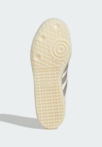 Suela de zapatilla de color claro con patrones de agarre texturizados, diseños circulares y ovalados, y un logo de marca en relieve.