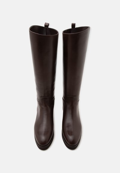 Paire de bottes hautes en cuir marron foncé avec bouts arrondis et languettes en haut, vues de dessus sur fond blanc.