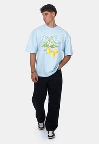 Světle modré oversized tričko s grafickým designem citronu a květin. Kombinováno s černými volnými kalhotami a černými teniskami.