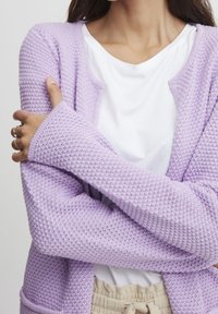 Ljuslila stickad cardigan med ett strukturerat mönster, öppen front och långa ärmar, lager på lager över en vit t-shirt.