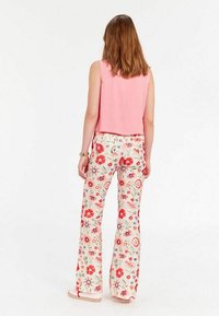 Un haut sans manches rose associé à un pantalon large à motif floral en crème, avec des fleurs rouges et bleues, offrant une coupe décontractée et une texture lisse.