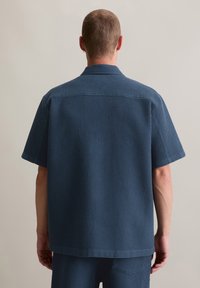 Kurzarmhemd aus strukturiertem, tiefblauem Stoff. Verfügt über einen Kragen und eine geradlinige Schnittführung, mit einem einfachen, klaren Design.