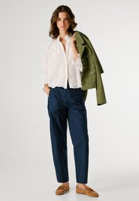 Λευκό μπλουζάκι με πλισέ μανσέτες, σκούρο μπλε φαρδιά παντελόνια και πράσινο στρατιωτικού στιλ πανωφόρι κρεμασμένο στο μπράτσο. Καφέ μοκασίνια.