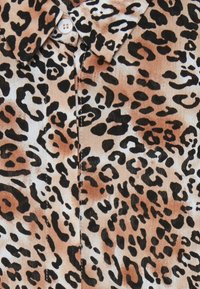 Tessuto stampa leopardo con una base marrone chiaro e macchie nere e marroni, colletto con bottoni, texture liscia e senza dettagli di cucitura visibili.