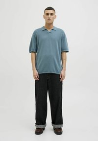 Polo shirt bleu clair avec un col classique, des manches courtes et une coupe décontractée, associé à un jean large foncé et des chaussures marron.