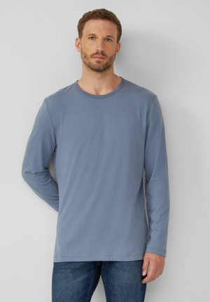 Langärmliges T-Shirt aus weichem blauen Baumwollstoff mit einem Rundhalsausschnitt, das eine glatte Textur und einen lässigen Schnitt bietet. Kombiniert mit dunklen Jeans.