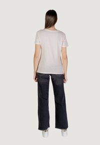 Maglietta di cotone rosa chiaro con maniche corte, abbinata a jeans larghi di denim scuri e sneaker chunky bianche, vista da dietro.