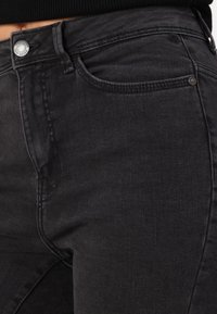 Los jeans de mezclilla negra presentan un diseño clásico con cierre de botón, bolsillos frontales y un acabado suave y ligeramente texturizado.