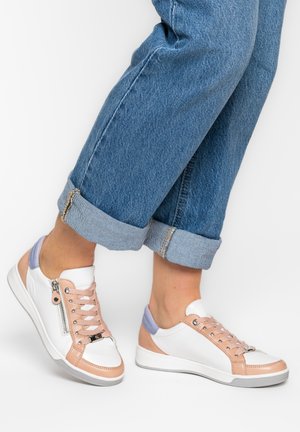 White sneakers with pale pink and lavender accents, side zippers, worn with rolled-up blue jeans on a white background.