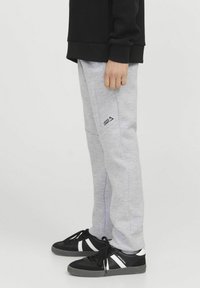 Szare dresowe spodnie o slim fit, z bocznymi kieszeniami i małym czarnym logo. Połączone z czarnymi tenisówkami i białymi paskami akcentującymi.