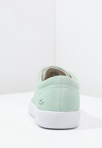 Světlé zelené semišové tenisky s bílou gumovou podrážkou. Na zadní straně je značková logo a embosovaný vzor. Hladké vnitřní podšívka.