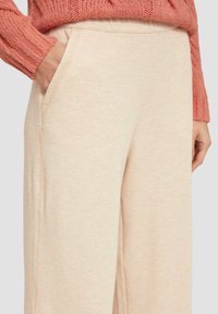 Beige wijde broek van zacht fabric met een gladde textuur. Bevat zijzakken en heeft een relaxte pasvorm. Zichtbare stiksels ter accentuering.