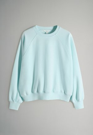 Bluza de culoare albastru deschis cu mâneci raglan, manșete și tiv nervurate. Textur ă netedă, decolteu rotund și design ușor adunat la mâneci.