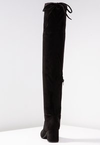 Černé kozačky nad kolena z měkké semišové kůže s kulatou špičkou, masivním podpatkem a nastavitelnými tkaničkami v horní části. Vypadá to, že mají boční zip.