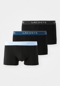 Black boxer shorts with elastic waistbands; one with gray, one with blue, and one with light blue accents featuring the Lacoste logo.