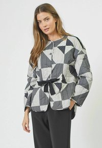 Prešívaná bunda s patchworkovým dizajnom v čiernej, bielej a sivej farbe s geometrickými vzormi, uväzovaním v páse a zapínaním na gombíky.