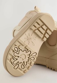 Beige gummisko sål med strukturerede grebsmønstre og et legende sprøjtedesign i midten, med glatte sider og en forstærket hæl.