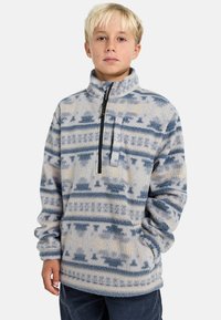 Fleece pulóver v svetlo modrej a krémovej farbe s geometrickým vzorom, polovičný zips na prednej strane, vysoký golier a dlhé rukávy. Mäkká textúra.