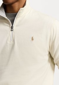 Pull negro de algodón con cuello alto, que cuenta con media cremallera y un logo bordado en beige en el pecho. Textura suave.