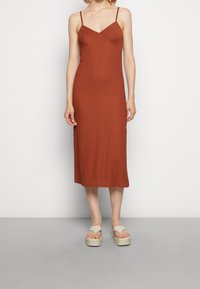 Ruusunvärinen, poimuinen midimekko ohuilla olkaimilla ja lyhyellä vartalolla; yhdistettynä beigeihin platform-sandaaleihin, joissa on leveät hihnat.