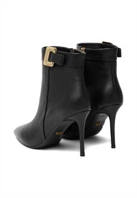 Mustad musta nahast kõrge kontsaga ankle boots, millel on teravad varbad, kuldsed pandlad ülaosas ja "GB" logo talladel.