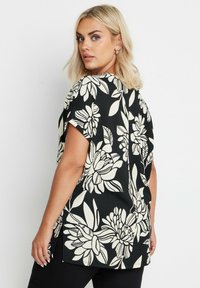 Blusa nera con fiori e maniche corte, con un motivo floreale crema, tessuto testurizzato e orlo posteriore leggermente più lungo.