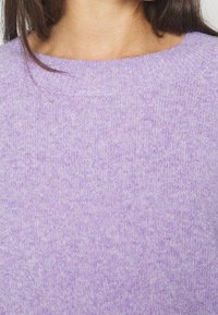 Lila stickad tröja med ribbat halslinne och mjuk textur. Tyget har ett subtilt melerat mönster som ger ett lätt utseende.