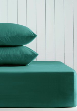 Dwa zielone poduszki ułożone na zielonym materacu na tle białej pionowej, paneled ściany.