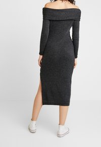 Robe en tricot grise à épaules dénudées avec des manches longues, fente jusqu'au genou, design ajusté et texture côtelée. Portée avec des baskets montantes blanches.